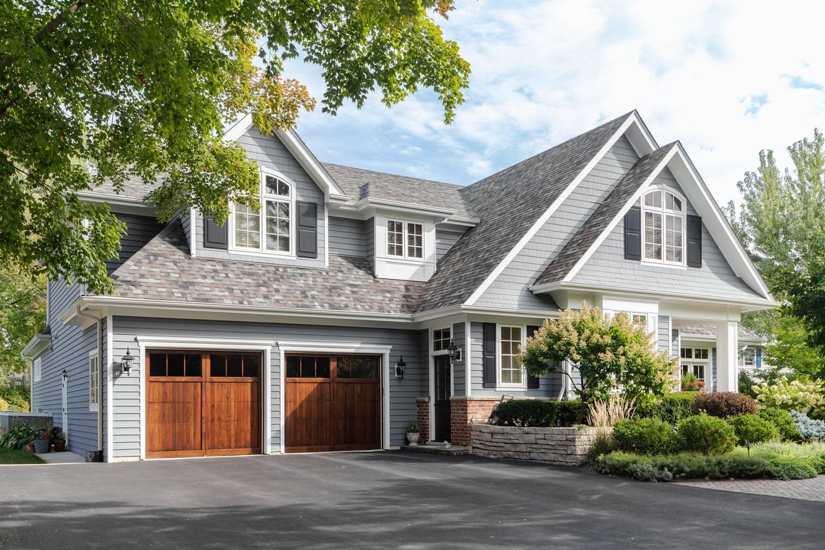 A grey and white farmhouse with two wooden garage doors and fresh landscaping