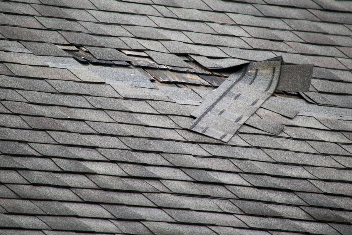 A badly damaged three-tab asphalt roof with missing shingles in need of repair